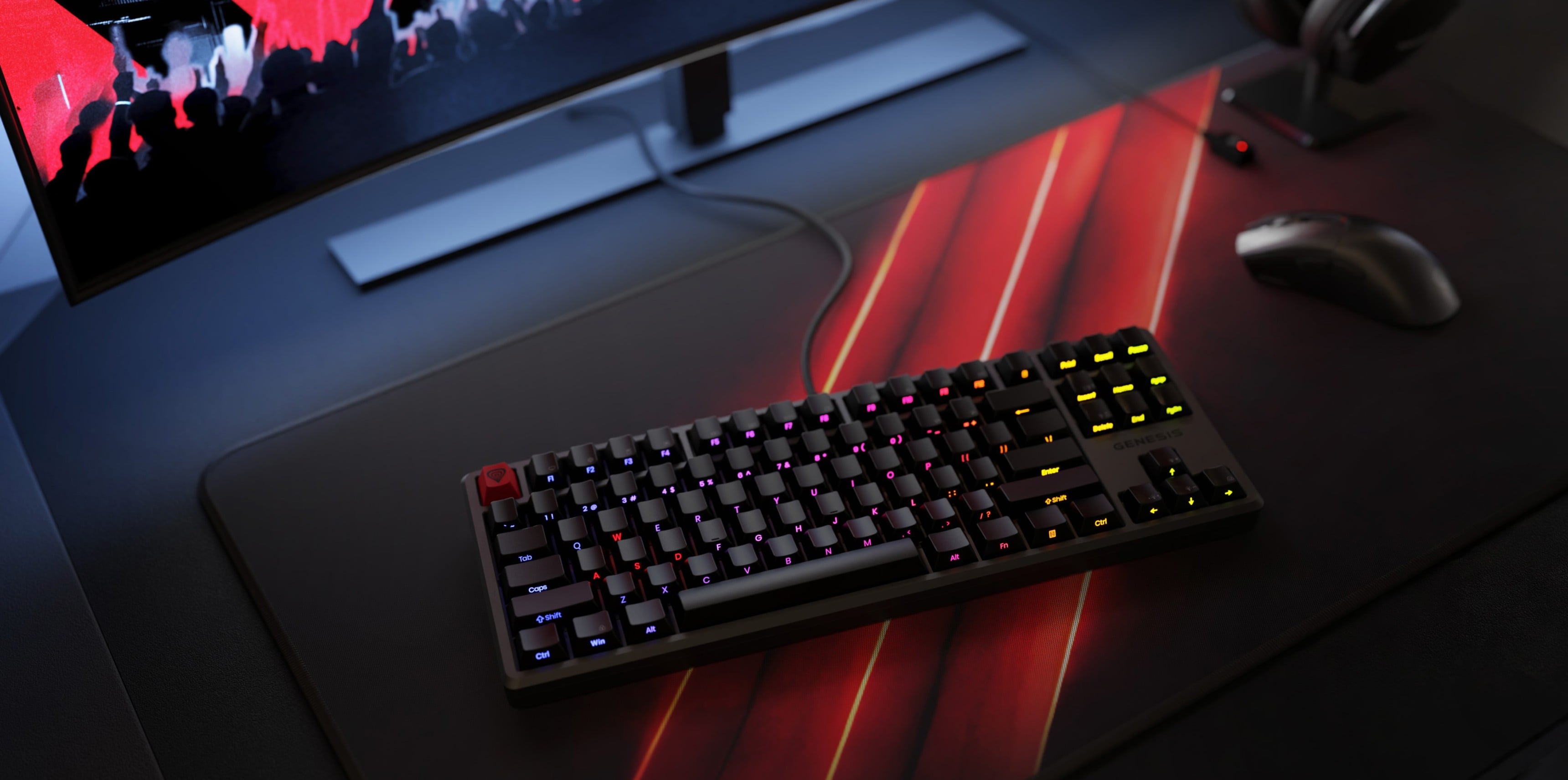 Keyboard with colorful backlighting on a gaming mouse pad next to a computer monitor.