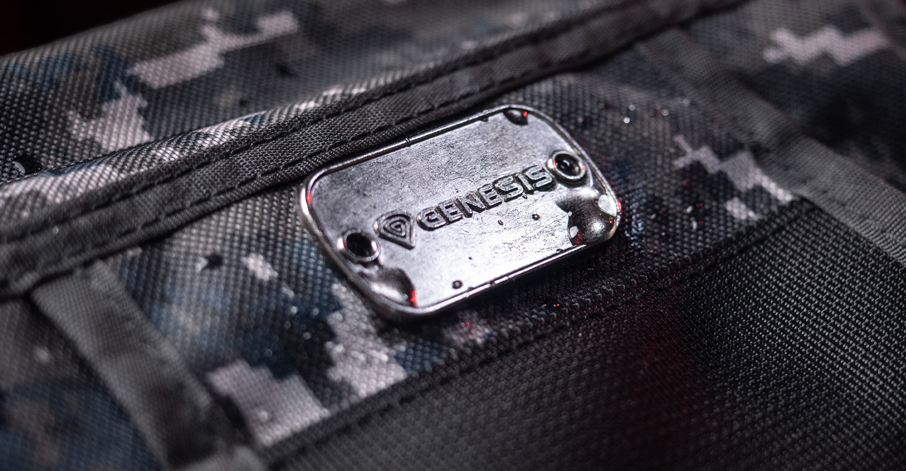 Close-up of the Genesis logo plate on the camo-patterned fabric of the Genesis Pallad 450 Lite laptop backpack