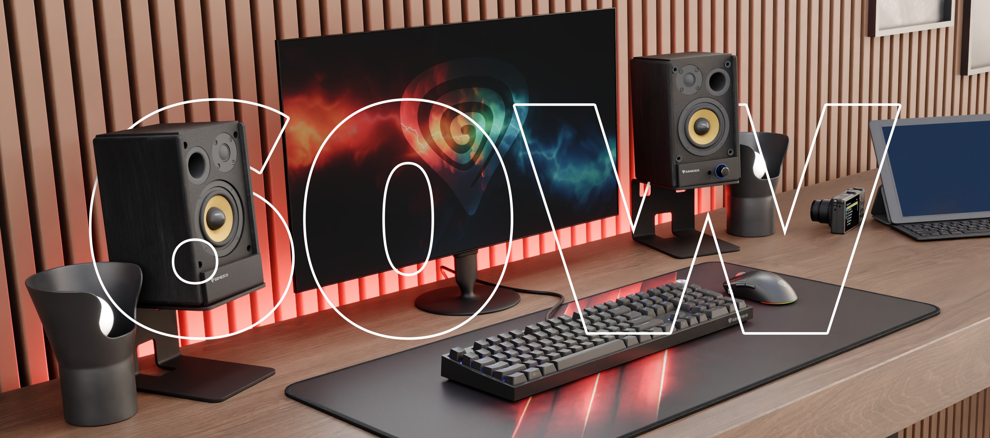 A desktop setup featuring a monitor, speakers, a keyboard, and a laptop with ambient lighting.