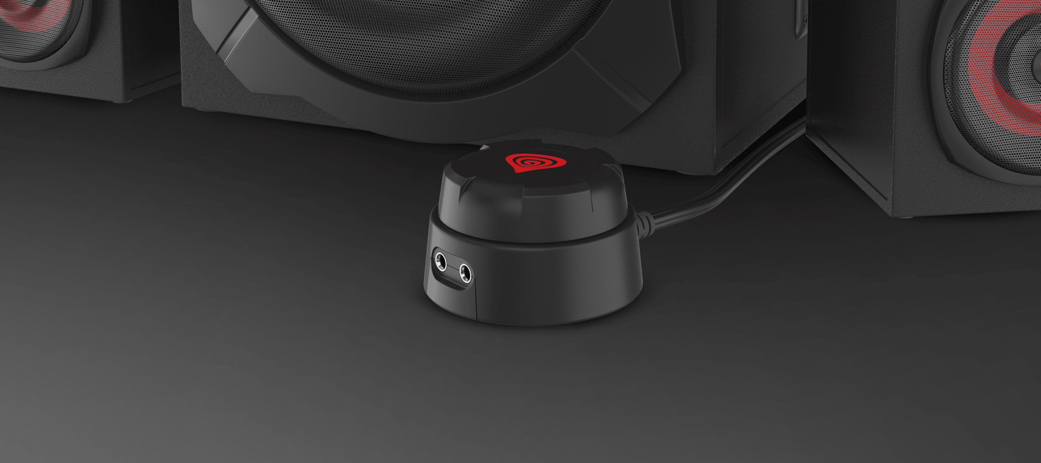 Black wired remote control for the Genesis Helium 610BT speakers, featuring audio inputs, positioned near the subwoofer