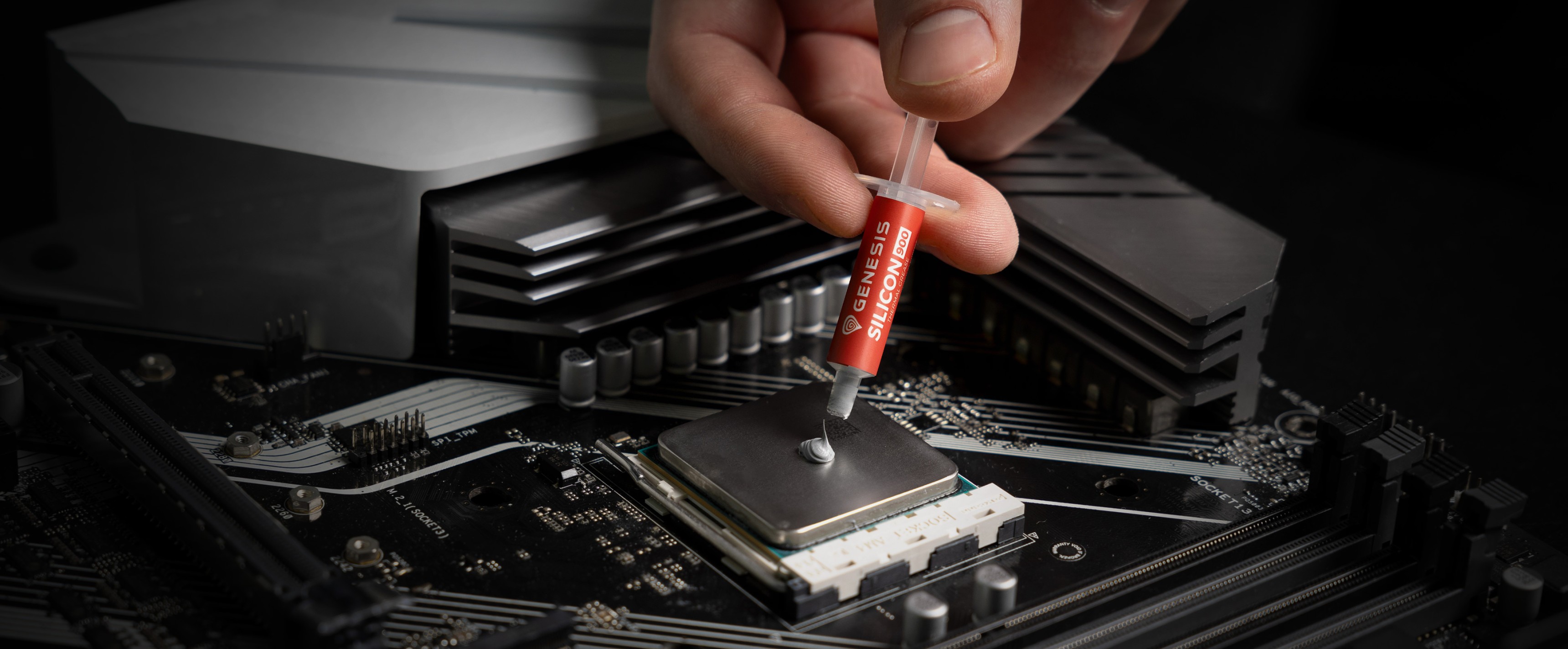 Hand applying thermal paste to a CPU on a motherboard, with a sleek computer cooling component in the background