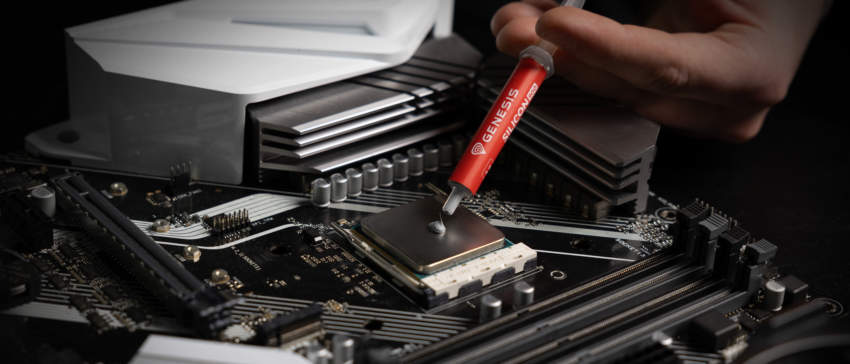 Applying Genesis Silicon 900 thermal paste onto a CPU socket on a motherboard for improved heat conductivity