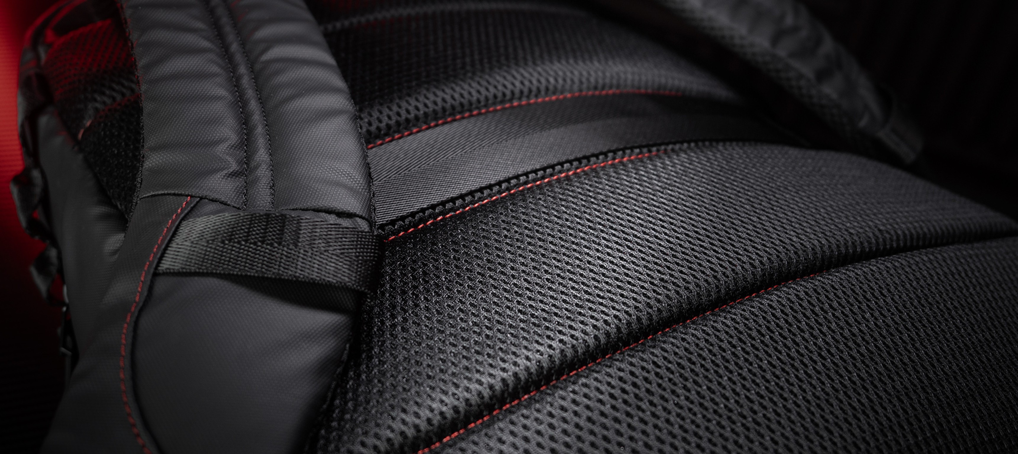 Close-up of the Genesis Pallad 420 backpack, showcasing its textured black fabric with red stitching and padded straps