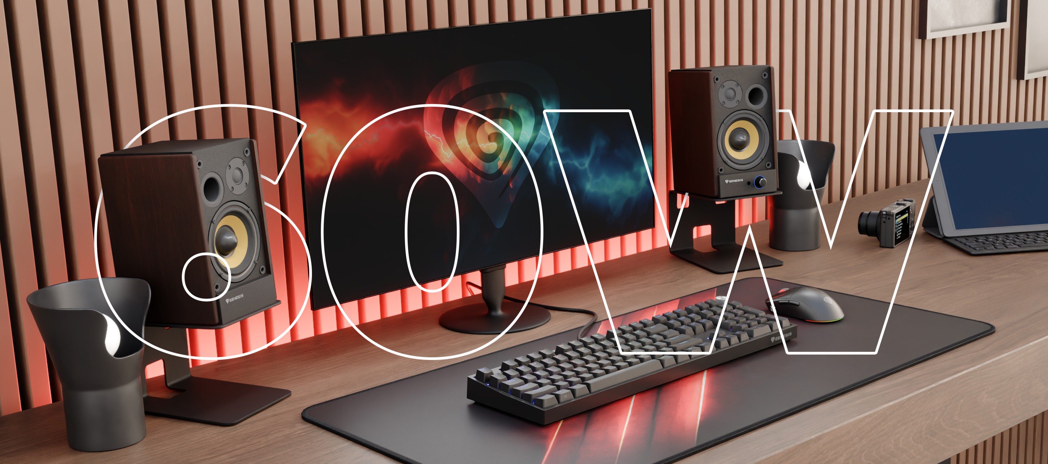 Desk setup featuring a monitor, keyboard, speakers, and a laptop on a wooden surface.