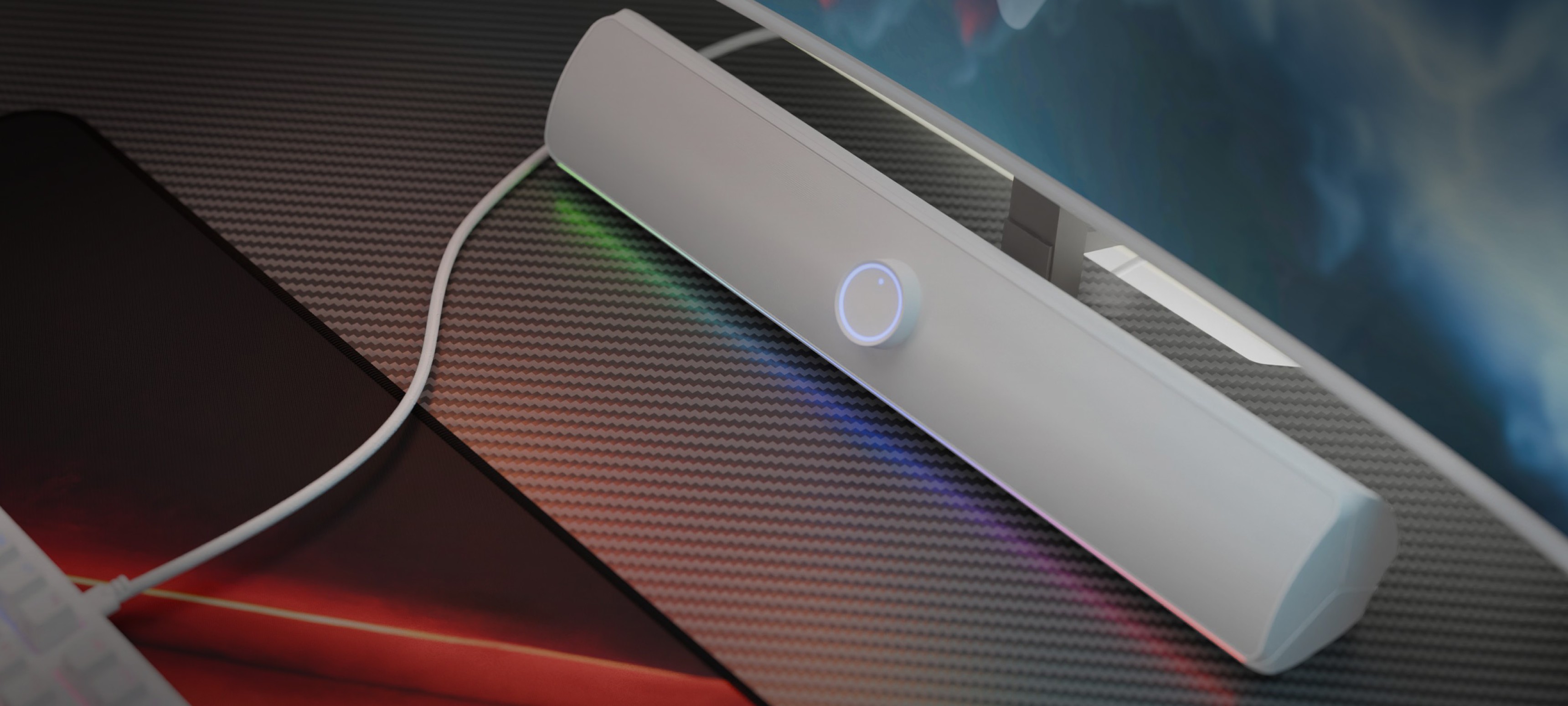 White Bluetooth soundbar with a glowing power button, placed on a textured surface beside a keyboard and monitor