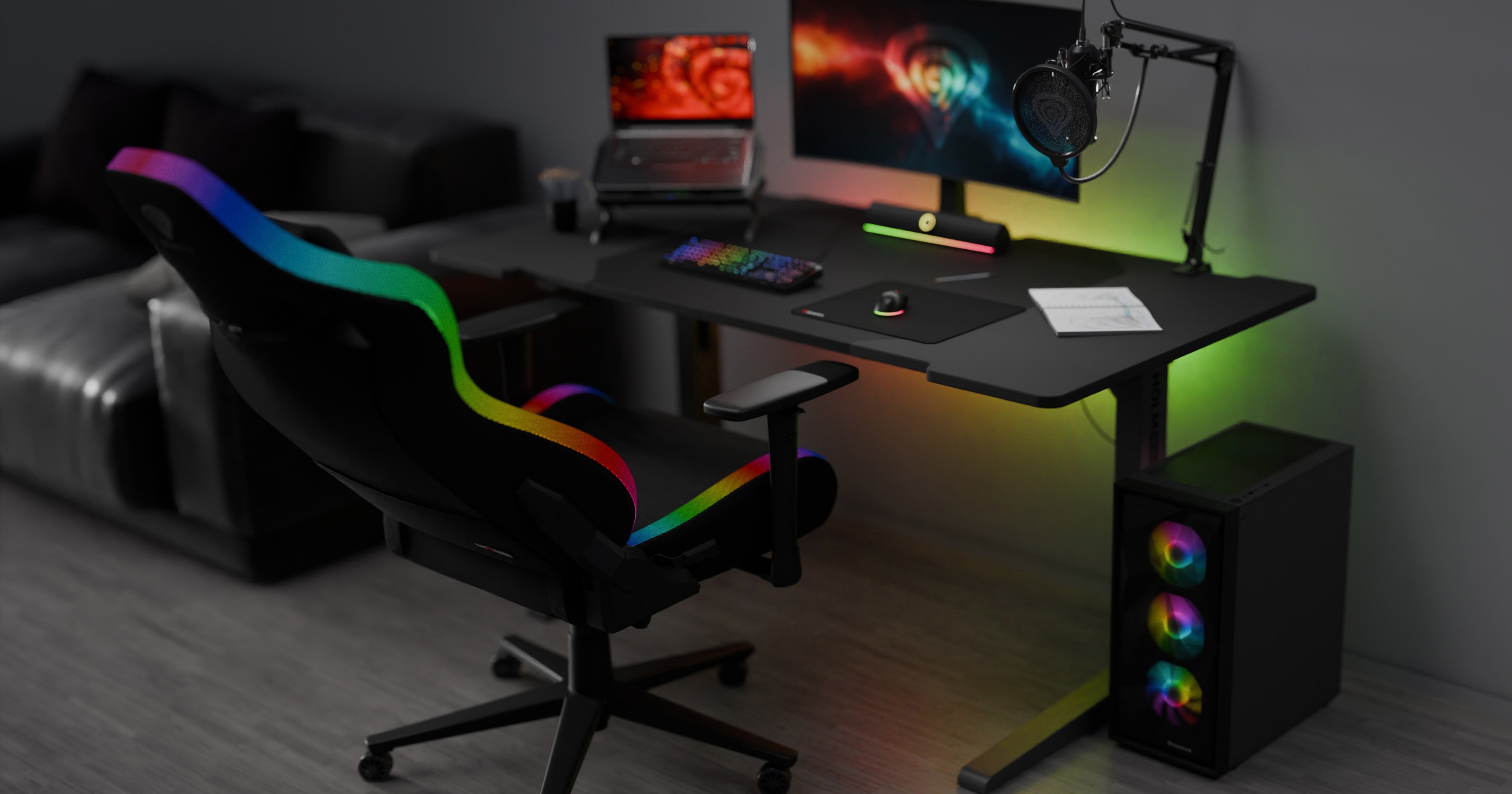 A black gaming chair with RGB accents is positioned next to a sleek desk with a monitor, keyboard, and colorful gaming setup