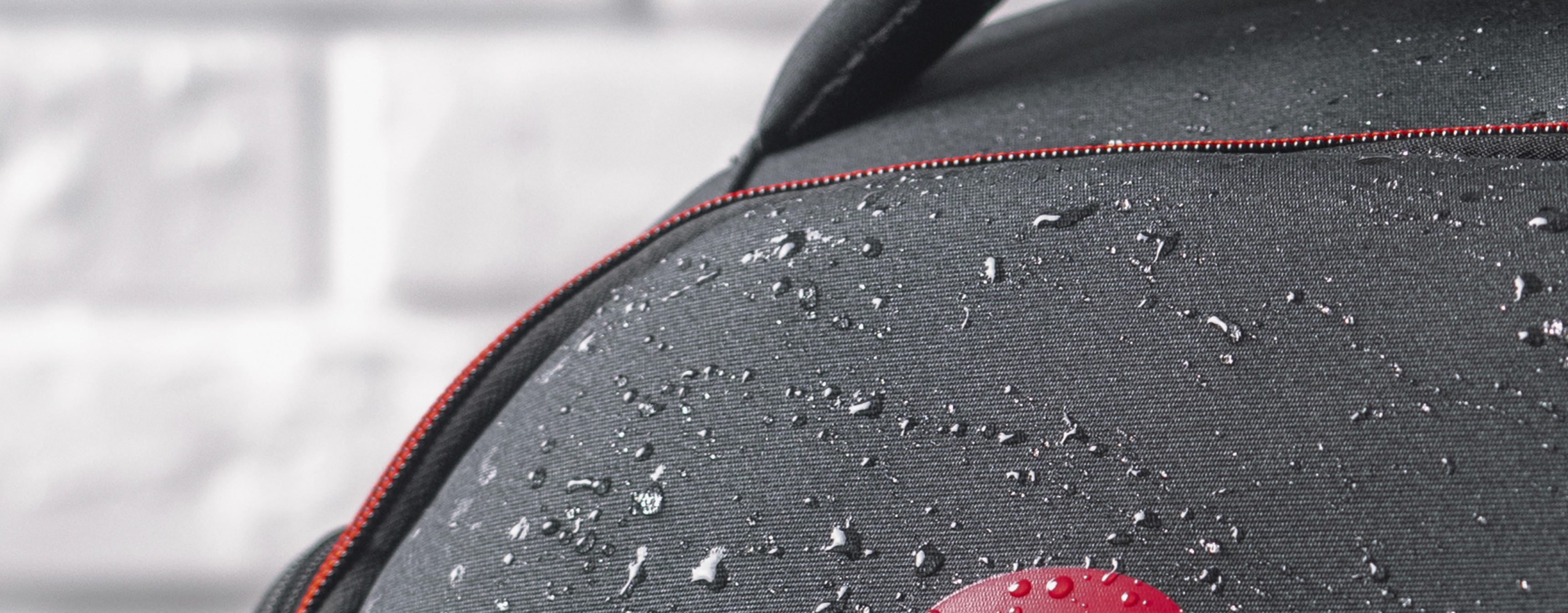 Water-resistant black laptop backpack with red accents, suitable for 15.6"/17.3" laptops, showing droplets on the fabric