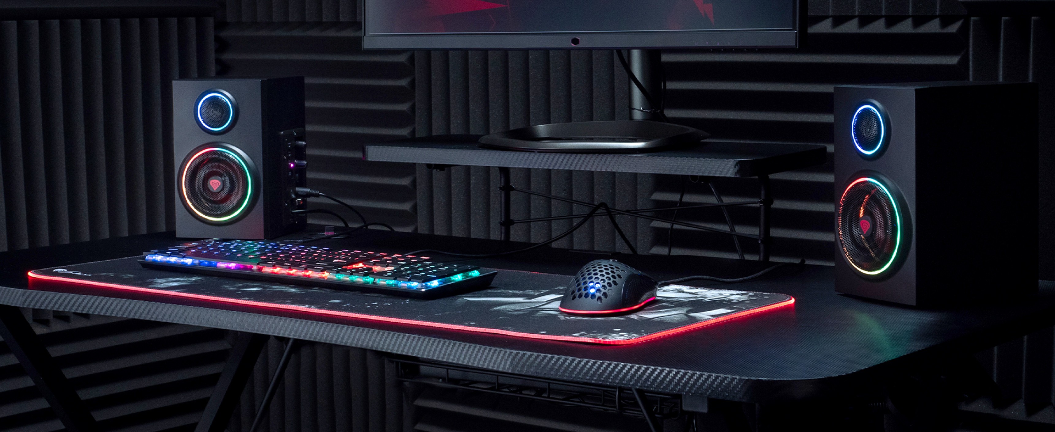 Bluetooth speakers with RGB lighting on a gaming desk, accompanied by a colorful keyboard and gaming mouse